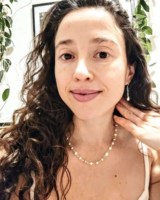 The maker wearing a white freshwater pearl necklace and pearl drop earrings