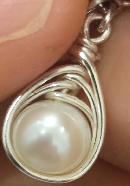 A pearl wrapped by hand in silver wire, held between two fingers